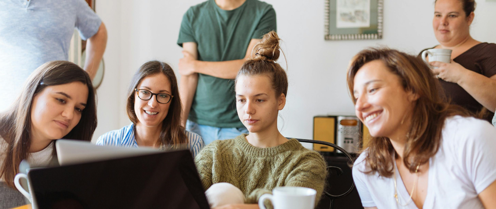 Ryhmä nuoria aikuisia istuu pöydän ääressä ja katsoo yhdessä kannettavan tietokoneen näyttöä. He hymyilevät ja keskustelevat rennosti etäyhteydellä.