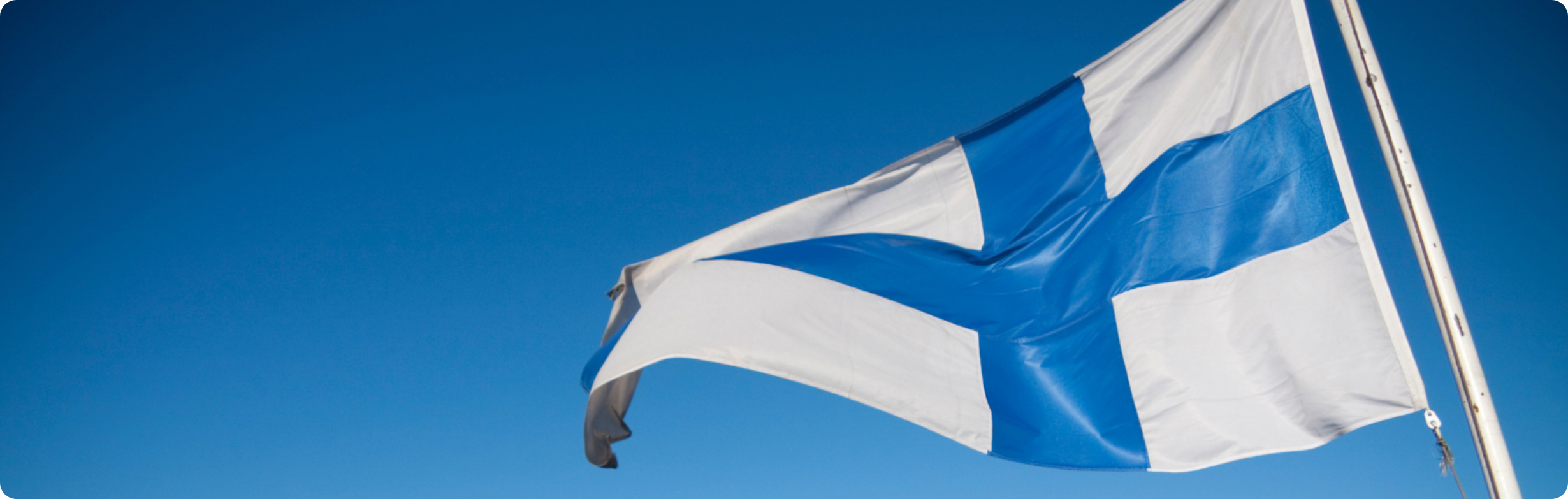 Suomen lippu liehuu sinistä taivasta vasten