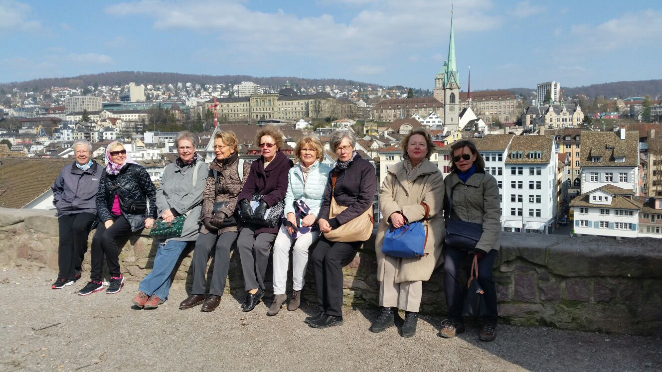 SenioriFoorum Zürichin osallistujia istumassa kaupunkinäkymän äärellä Zürichissä; taustalla näkyvät vanhakaupunki ja kirkontorni.