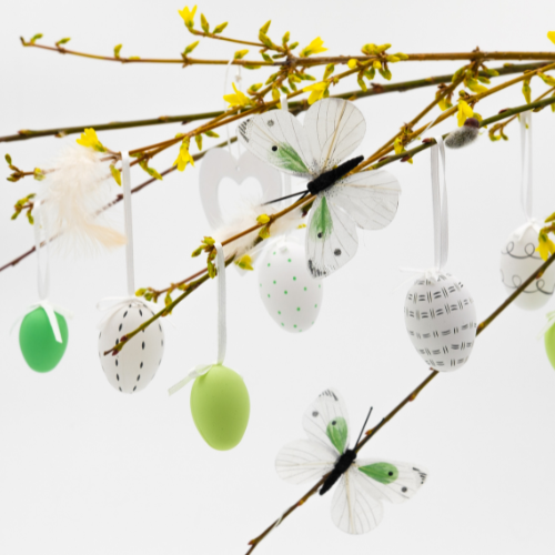 Pajunoksille ripustettuja pääsiäismunia ja paperiperhosia vaalealla taustalla, keväinen suomalainen pääsiäiskoriste.